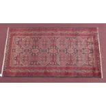 A North East Persian Meshad Belouch rug, repeating stylised geometric motifs on a rouge field,