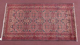 A North East Persian Meshad Belouch rug, repeating stylised geometric motifs on a rouge field,