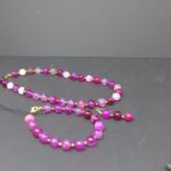A gilt metal and polished pink banded agate suite to include bead necklace, bracelet and pair of