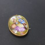 A Victorian 9ct gold and hand painted porcelain brooch, decorated with a man playing the violin to a