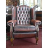 A 20th century stud bound button back leather wingback armchair, raised on cabriole legs