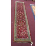 A North-West Sarouk runner, repeating stylised floral motifs on a rouge field, complimented by a