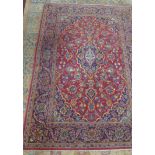 A Kashan carpet with central floral medallion surrounded by floral motifs, on a red ground,