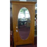 A French walnut armoire with inset bevelled oval mirror plate to door, enclosing adjustable