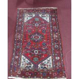 A 20th century Hamadan rug with geometric medallion, surrounded by motifs on a red ground, contained