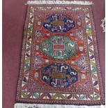 A 20th century Iranian Kazak rug with 3 geometric medallions, on a red ground, contained by
