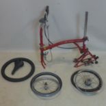 A red Brompton folding bicycle lacking pedals