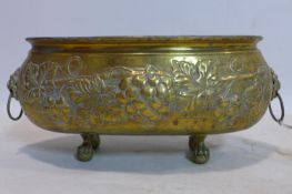 An oval brass planter, repousee embossed with grape vines, having lion head ring handles, on claw