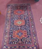 An antique Kazakh carpet with 3 geometric medallions, surrounded by geometric motifs on a blue