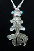 A white metal pendant necklace modelled as a fish with turquoise eyes, L.8cm (pendant)