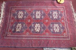 A 20th century Afghan carpet with 6 geometric medallions, on a red ground, contained by many