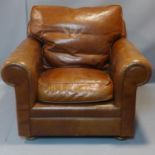 A club armchair upholstered in tan leather on turned mahogany bun supports. W.95cm