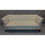 A sofa in pale grey buttoned upholstery on square tapering supports. H.86 W.223 D.90cm