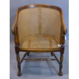 A mahogany bergere armchair, with cane panel seat and backrest, with scrolling arms, on turned