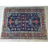 A Caucasian rug with geometric and floral motifs on a dark blue ground, within stylised floral