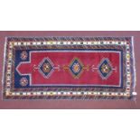 A Persian Shirvan rug, triple diamond medallion on a rouge field, within blue and cream border,