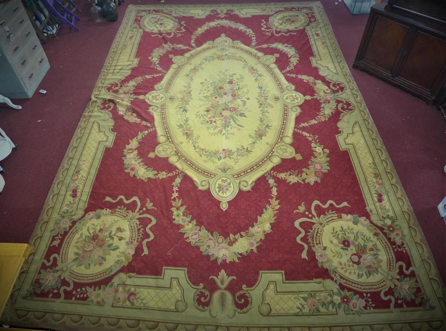 A large needlepoint carpet with central floral medallion and floral motifs on a red ground, within