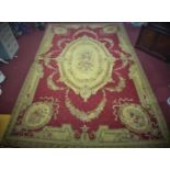 A large needlepoint carpet with central floral medallion and floral motifs on a red ground, within