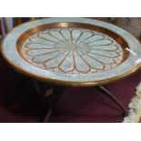 A large Middle Eastern copper tray top table, having ornate scrolling foliate decoration, on folding
