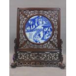 A Chinese padouk wood carved screen with a porcelain blue and white panel depicting ?silk