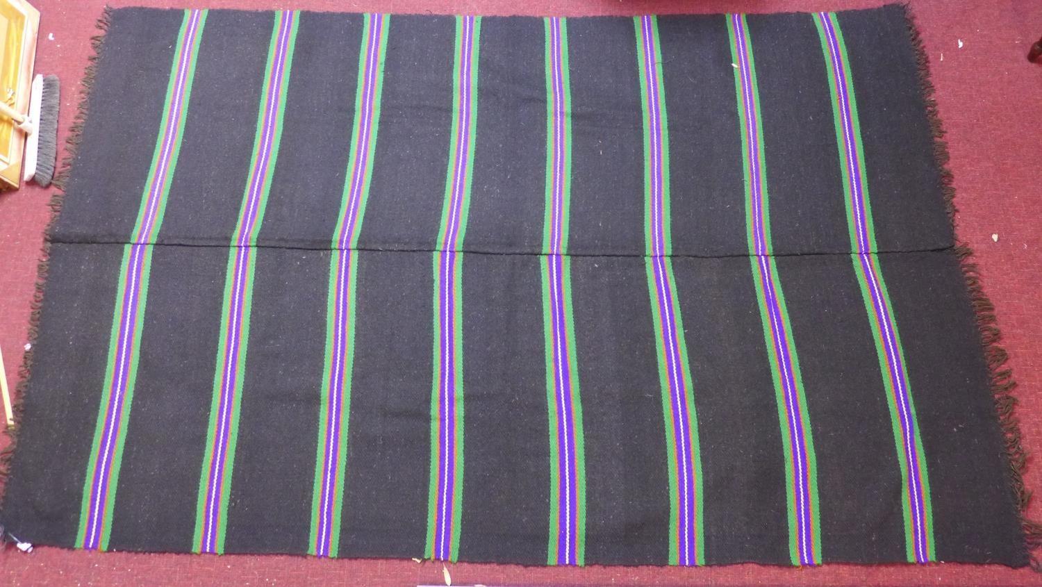 A woollen rug with purple, green, yellow and orange stripes on a black ground, 223 x 143