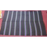 A woollen rug with purple, green, yellow and orange stripes on a black ground, 223 x 143
