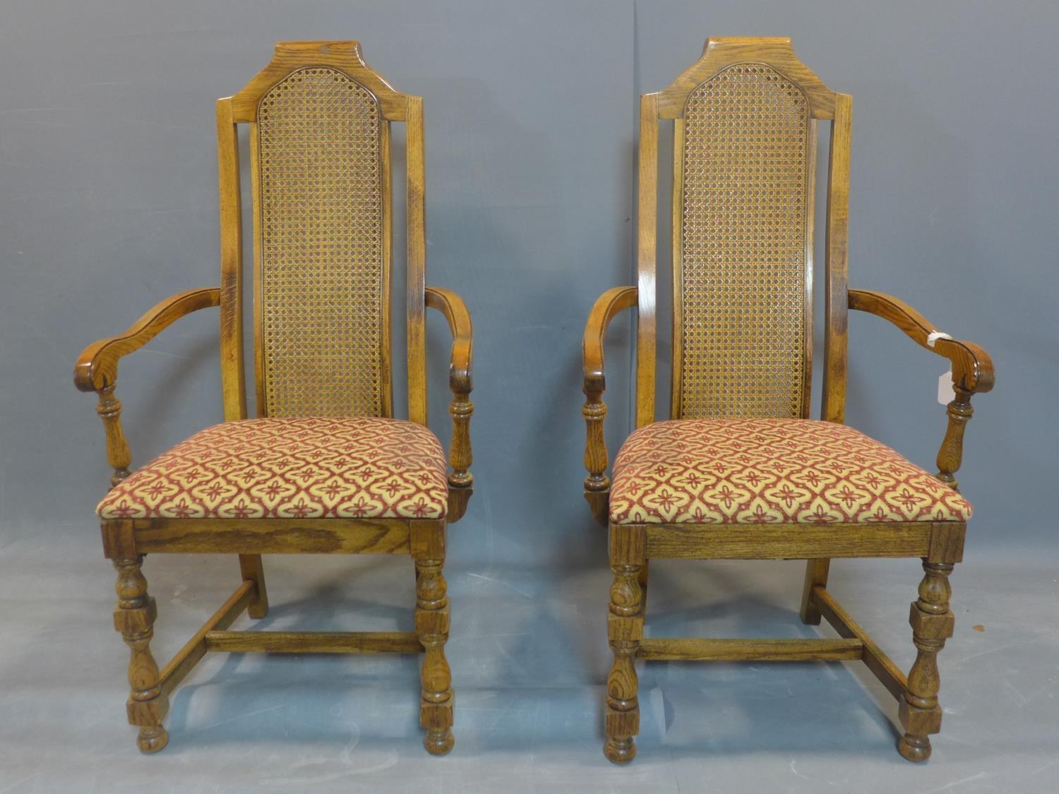 A pair of fruitwood and rattan carver armchairs, with caned backs, raised on turned legs joined by