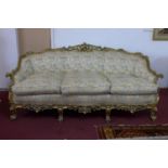 A three seater giltwood settee, with elaborate c-scroll and floral carved giltwood frame, on c-