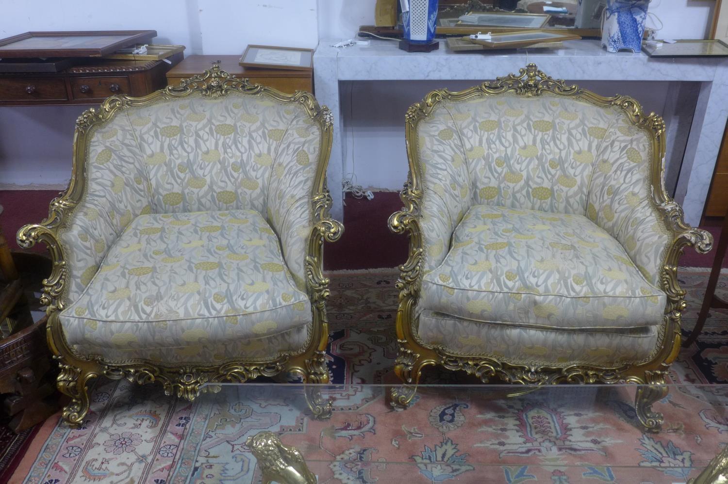 A pair of giltwood armchairs, with elaborate c-scroll and floral carved giltwood frames, on c-scroll