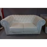 A two seater Chesterfield sofa upholstered in faux white leather