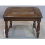 An early 20th century mahogany sloped stool, with caned seat, raised on turned legs joined by