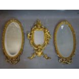 A pair of oval gilt wall mirrors with ribbon and C-scroll decoration to frames, having bevelled