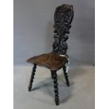 An 18th century oak spinning chair, the backrest carved with scrolling foliage, dog's heads, and