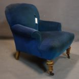 A Victorian armchair with blue velour upholstery, raised on turned legs and castors