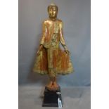 A large Burmese carved wood Buddha standing on a lotus base, gilt painted with cut glass
