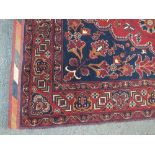 AN EARLY / MID 20TH CENTURY WOOLLEN RUG / CARPET, on a dark red ground with striped edging, 290 x