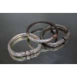 THREE ORIENTAL WHITE METAL BANGLES, one being a half whalebone example