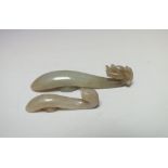 TWO CHINESE CELADON JADE BELT HOOKS, of plain form with carved mythical dragon head to one end,