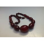 A SINGLE STRAND OF VINTAGE GRADUATED CHERRY AMBER BEADS, with damages, central bead Dia. 2 cm,