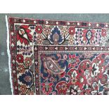 AN EASTERN WOOLLEN RUG / CARPET, with an all over floral swirling pattern on a mainly red ground,