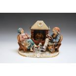 A CAPO DI MONTE MEDEA FIGURE OF AN OLD COUPLE SITTING BY THE FIRESIDE, W 29.5 cm