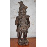 West African carved wood figure carrying wicker fish tap on his back, a seashell slung over his
