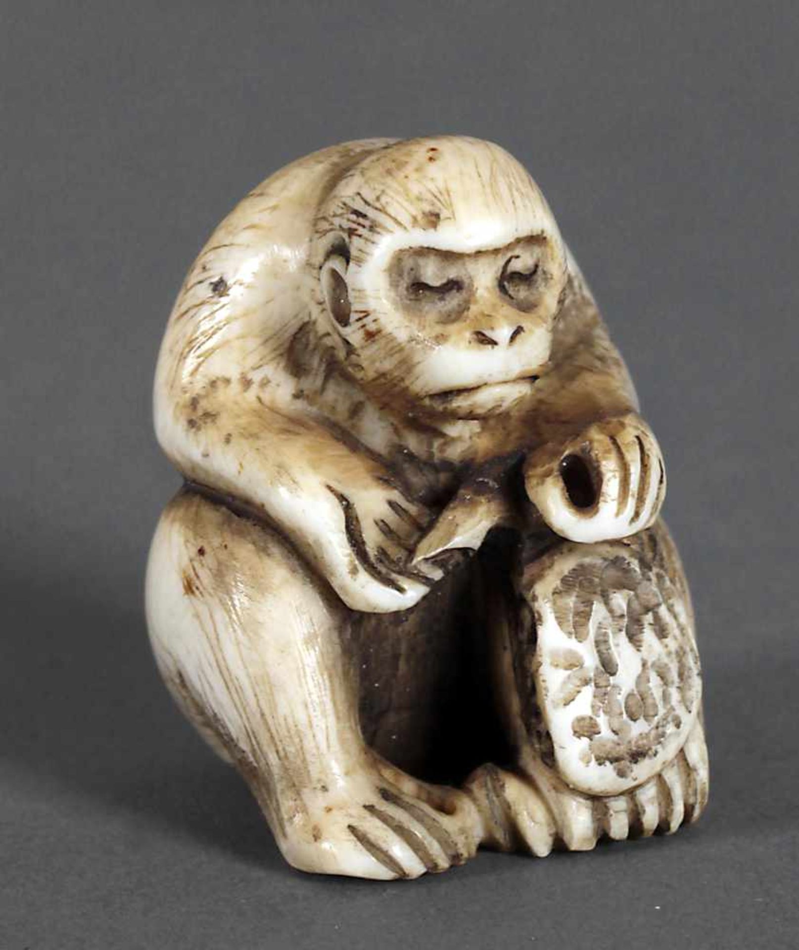 Netsuke eines sitzenden Affen, 19. Jh.der ein Instrument (?) bedient, das an seinem linken Bein