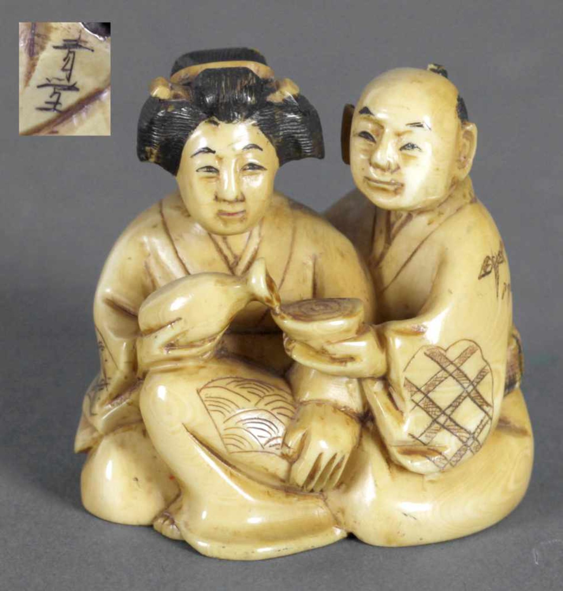 Netsuke eines Paares in Sitzposition, 19. Jh.Elfenbein gelb patiniert, er reicht mit der linken Hand