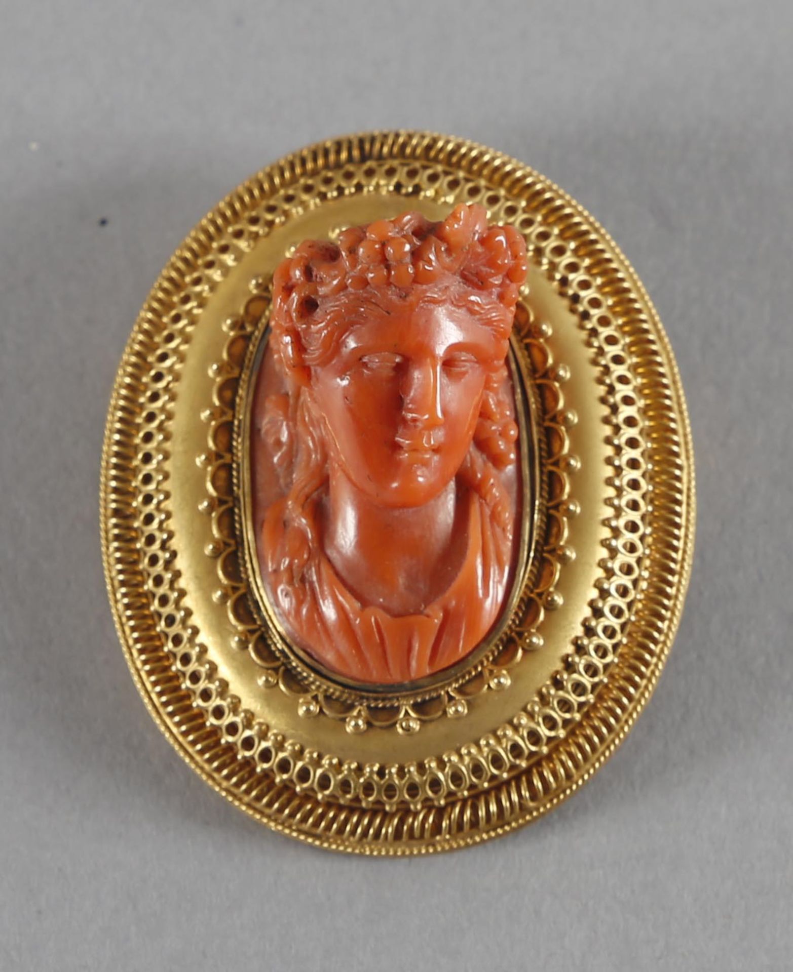 Fein verzierte Brosche aus 18 kt Gold, antikisierende Frauenbüste mit Weinlaub im Haar, rote