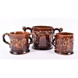 A collection of three Staffordshire treacle-glazed frog mugs comprising two loving cups and one with