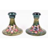 A pair of William Moorcroft candlesticks of squat form, with tube-lined floral decoration on a green