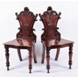 A pair of 19th century mahogany hall chairs with scroll bordered backs and central stylised shell