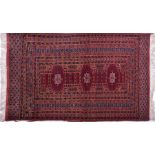 A small Afghan fringed wool rug the burgundy ground decorated with medallions in shades of orange,