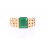 A yellow metal, diamond, and emerald ring set with an emerald-cut emerald, the stepped shoulders